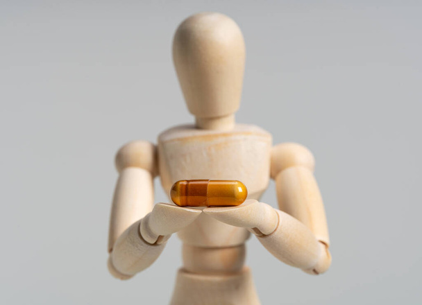 Dřevěná figurína s pilulkami na bílém pozadí. Koncepce léčiv a doplňků. - Fotografie, Obrázek