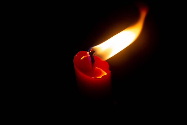 Красная свеча с желтым пламенем на черном фоне - Фото, изображение