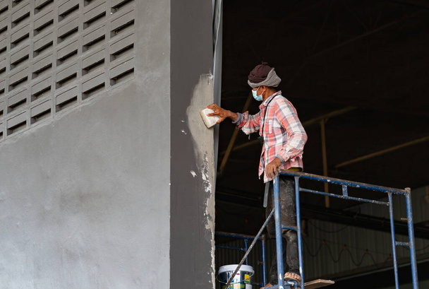 Vakolat csiszolása az újonnan vakolt felületén egy szürke fal alatt rögzített előkészítése festés egy magas falú gyárban. - Fotó, kép