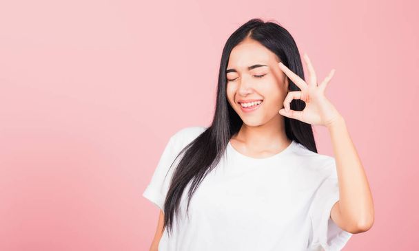 Portrait Asian beautiful young woman made finger OK symbol sign gesture wink eyes to agree and looking at camera, studio shot isolated on pink background, Thai female agree hand sign copy space - Photo, Image
