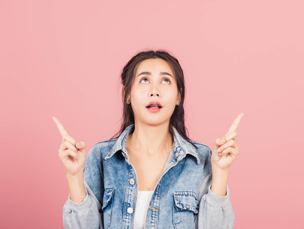 Asian happy portrait beautiful cute young woman wear denim standing makes gesture two fingers point upwards above presenting product something, studio shot isolated on pink background with copy space - Foto, Imagen