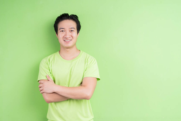 Portret van Aziatische man in groen t-shirt poseren op groene achtergrond - Foto, afbeelding