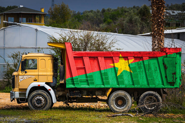 Camião basculante com a imagem da bandeira nacional de Burkino Faso está estacionado no fundo do campo. O conceito de exportação-importação, transporte, entrega nacional de mercadorias - Foto, Imagem