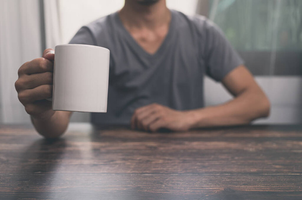 Muž držící sklenici vody, hrnek na kávu, na stole, ve své kanceláři. - Fotografie, Obrázek