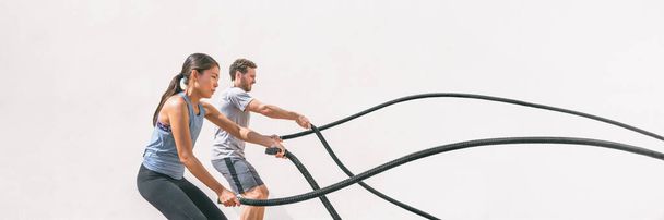 Gym fitness sport fit couple working out battle rope exercise banner panorama. Woman and man cross training amrs muscles and cardio with battling rope. Core workout panoramic crop - Fotografie, Obrázek