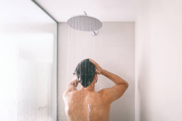 Man taking a shower washing hair with shampoo product under water falling from luxury rain shower head. Morning routine luxury hotel lifestyle guy showering. body care hygiene - Foto, afbeelding