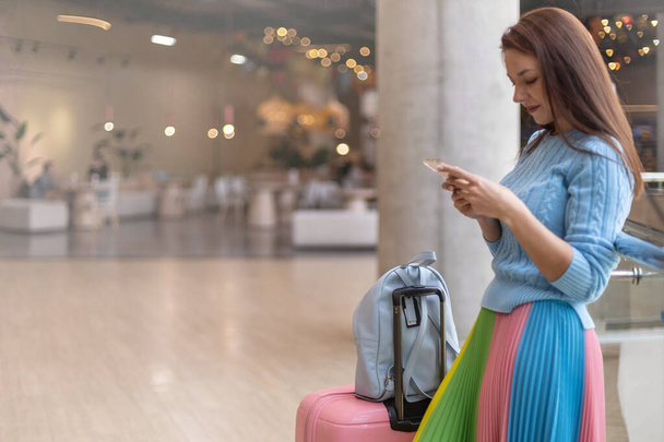 Happy elegant travel woman with baggage standing at duty free shopping mall relaxing use smartphone - Foto, immagini