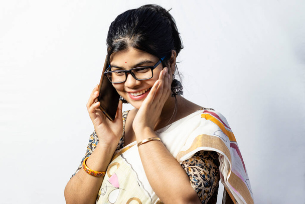 Una hermosa mujer india en saree hablando por teléfono inteligente y sonriendo aislada sobre fondo blanco - Foto, Imagen