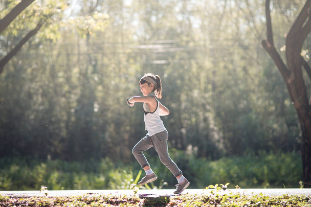 Счастливая девочка бегает летом в парке на природе. теплый солнечный свет вспышки. Азиан Литтл бегает в парке. спорт на открытом воздухе и фитнес, упражнения и обучение конкуренции для развития ребенка. - Фото, изображение