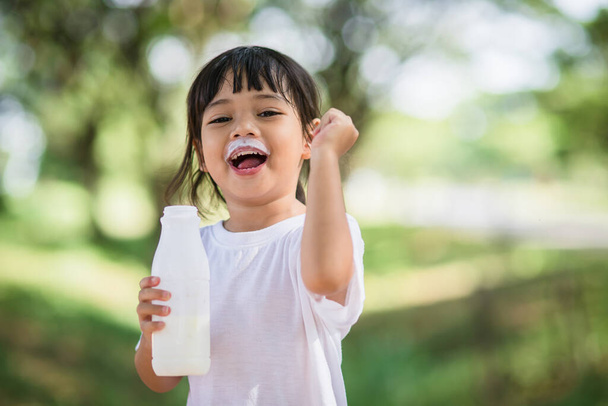 Милая азиатская маленькая девочка пьет молоко, мягкий фокус - Фото, изображение