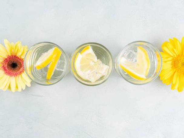 Bebida de agua de limón con cubitos de hielo sobre fondo de piedra con flores amarillas gerberas - Foto, Imagen