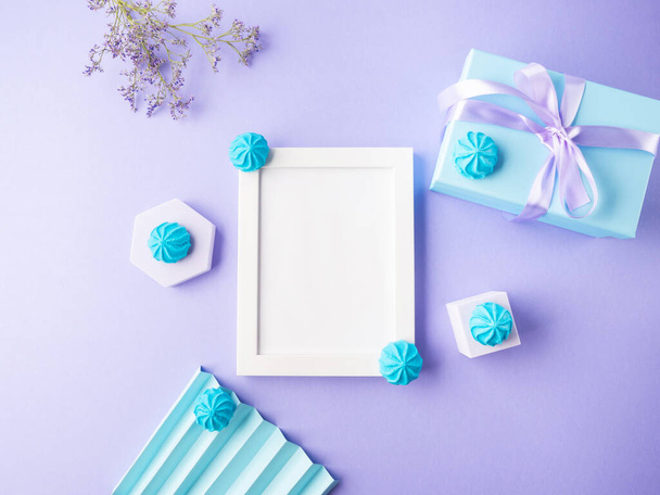 Biała pusta ramka na fioletowym tle z niebieskim słodkim wystrojem, świąteczne płaskie leżaki - Zdjęcie, obraz