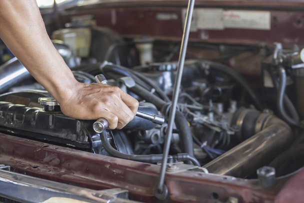 De hand van een man die de motor van een kapotte auto repareert - Foto, afbeelding