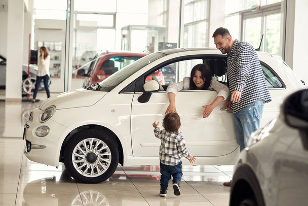 The manager helps the young family choose the most comfortable car for the city. - Foto, imagen