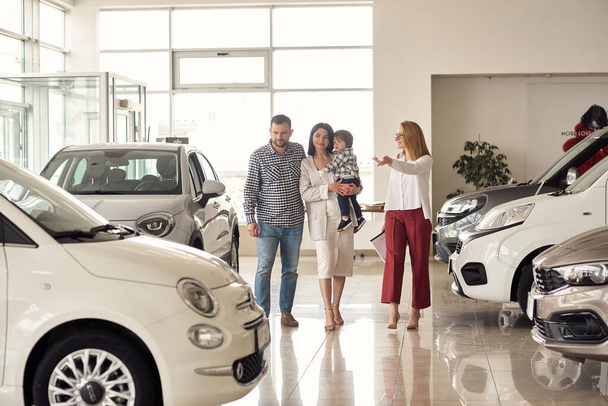 The manager helps the young family choose the most comfortable car for the city. - Фото, изображение