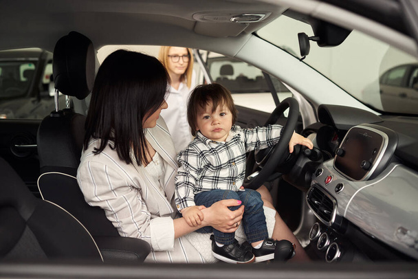 El gerente ayuda a la joven familia a elegir el coche más cómodo para la ciudad. - Foto, imagen