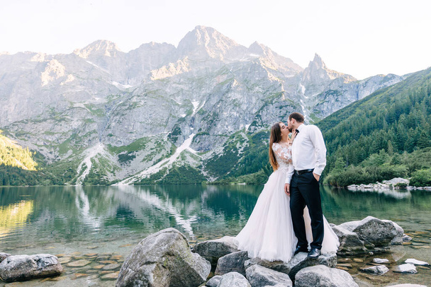 岩の海岸に立つ愛のロマンチックな結婚式のカップル。絵のように美しい山の景色. - 写真・画像