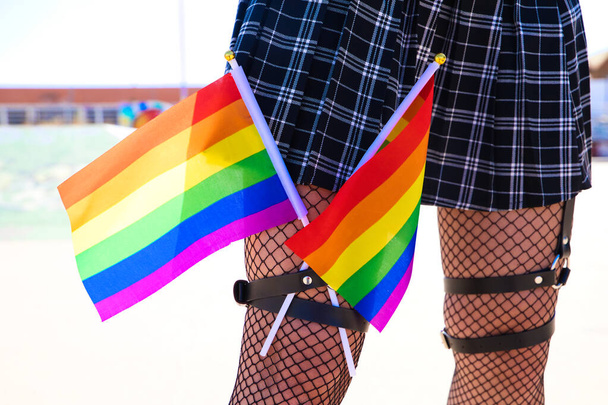 girl's leg detail with fishnet stockings and leather garters on which you can see two gay pride flags intertwined with each other. Concept gay lesbian freedom and rights. - Foto, afbeelding