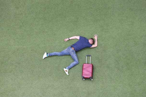 Człowiek nieruchomy leży na zielonym trawniku z walizką - Zdjęcie, obraz