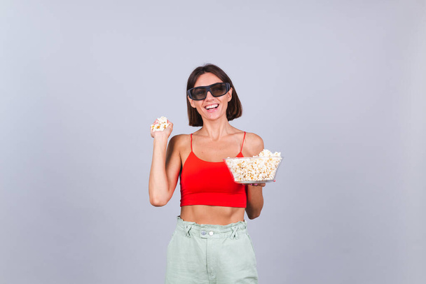 Mooie vrouw op grijze achtergrond in 3D bioscoop bril met popcorn, vrolijke vrolijke positieve emoties - Foto, afbeelding