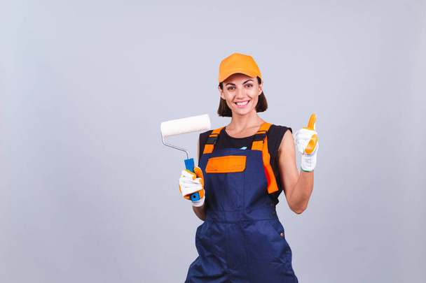 Mulher pintor com escova de rolo no fundo cinza sorriso positivo mostra polegar alegre - Foto, Imagem