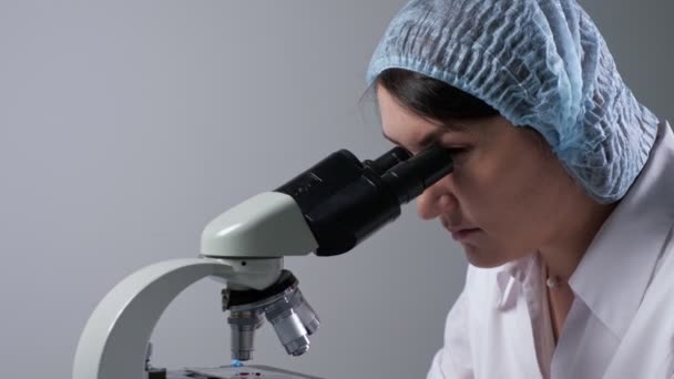 Assistente de laboratório olha para a amostra de material através do microscópio - Filmagem, Vídeo