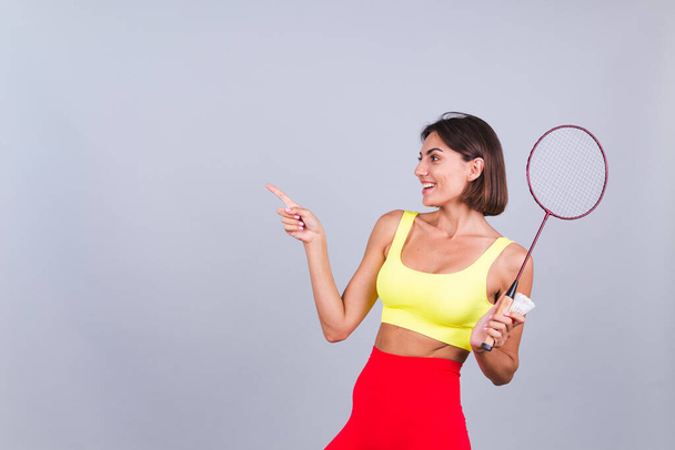 Fit žena ve sportovním oblečení top a legíny držet badminton raketa šťastný pozitivní veselý show bod vlevo s prstem na prázdné místo - Fotografie, Obrázek