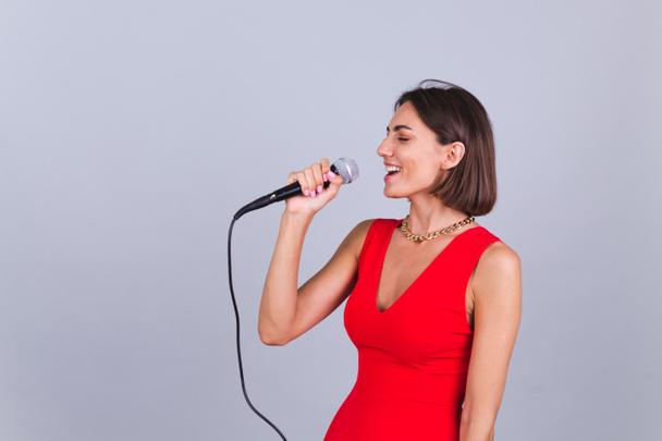 Beautiful woman on gray background with microphone singing romantic favorite love song with eyes closed - Photo, Image