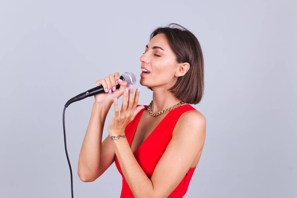 Gri arka planda güzel bir kadın mikrofonla en sevdiği romantik aşk şarkısını söylüyor gözleri kapalı - Fotoğraf, Görsel