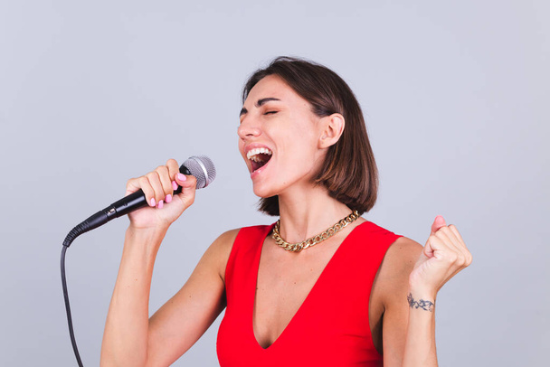 Kaunis nainen harmaalla taustalla mikrofoni laulaa emotionaalinen suosikki laulu onnellinen positiivinen iloinen - Valokuva, kuva
