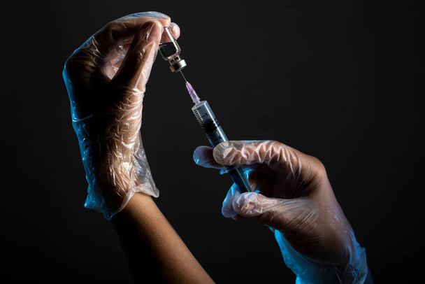 manos que sostienen la jeringa y el frasco de vacuna aislados en negro - Foto, imagen
