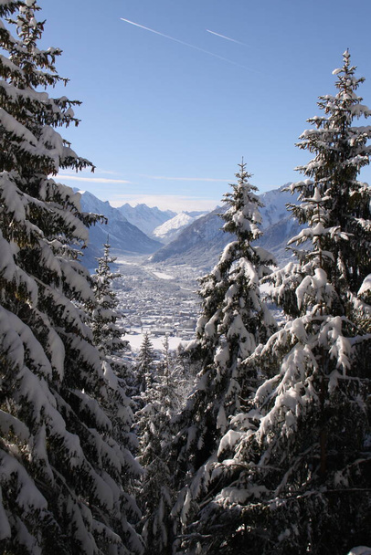 Blick von oben auf eine schneebedeckte Alpenstadt durch ein paar schneebedeckte Evergreens - Foto, Bild