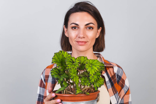 Gyönyörű nő kockás ing szürke háttér tartja növény a kezében, kert koncepció boldog pozitív mosoly - Fotó, kép