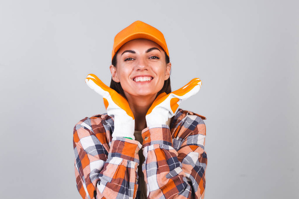 Hermosa mujer en camisa a cuadros, sombrero y guantes sobre fondo gris feliz emocionado alegre casa de reparación listo - Foto, Imagen