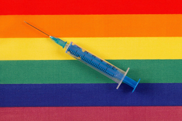 Medyczna jednorazowa, jałowa, niebieska strzykawka z przezroczystego tworzywa sztucznego z wyjmowaną igłą na tle tęczowej flagi LGBT. Zatrzymanie AIDS (ludzki wirus niedoboru odporności, HIV) - Zdjęcie, obraz