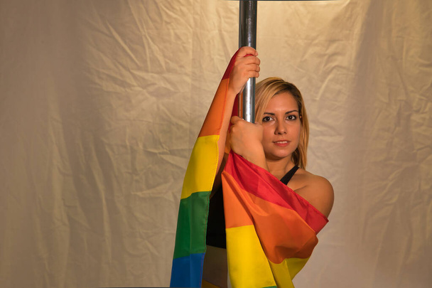Femme danseuse de pole avec un drapeau gay pride autour de son corps accroché sur le poteau. Position horizontale. - Photo, image