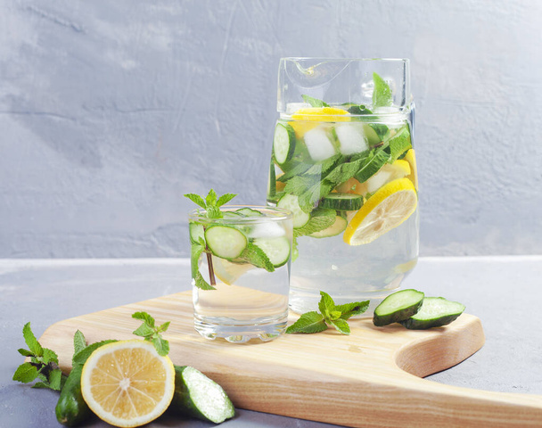Health care, fitness, healthy food concept. Fresh cool mint lemon cucumber pour water, cocktail, detox drink, lemonade in a glass jug. - Fotó, kép