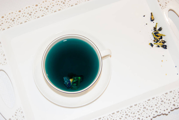 Kolor nastroju jest niebieski - niebieska herbata w białym kubku, który stoi na białym spodku i białej tacy. Przydatne napoje, właściwości lecznicze. Fitoterapia. Impreza herbaty. - Zdjęcie, obraz
