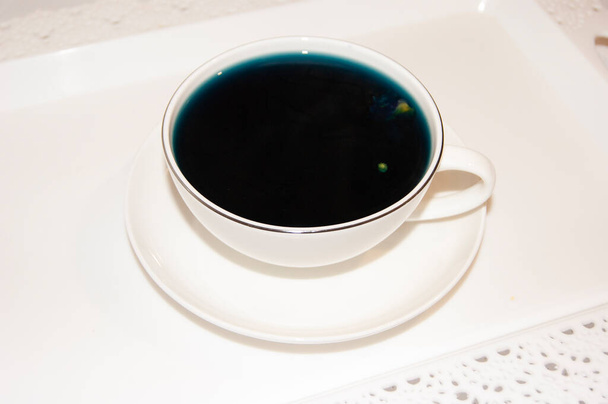 Die Stimmungsfarbe ist blau - blauer Tee in einem weißen Becher, der auf einer weißen Untertasse und einem weißen Tablett steht. Nützliche Getränke, heilende Eigenschaften. Phytotherapie. Tea party. - Foto, Bild