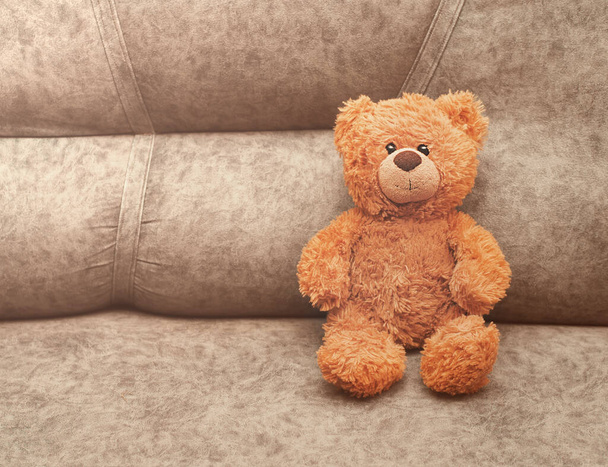 pluszowy miś zabawka siedzi na kanapie i patrzy na widza. koncepcja bezpieczeństwa i samotności dzieci. dzieci najlepszy przyjaciel. - Zdjęcie, obraz