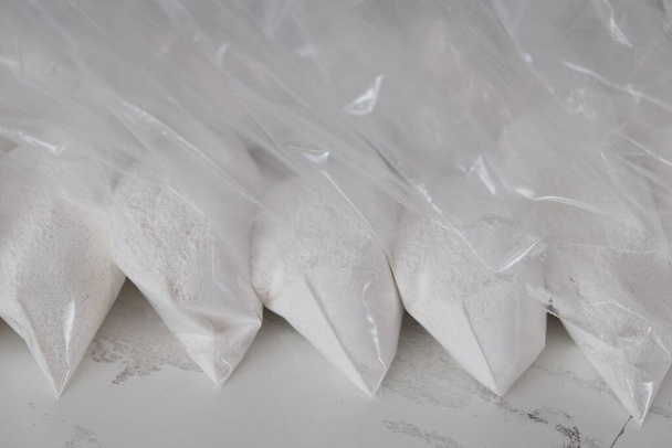 Μεγάλος αριθμός διάφανων φακελλίσκων γεμισμένων με λευκή σκόνη. Λευκή σκόνη συσκευασμένη σε μικρά φακελάκια. - Φωτογραφία, εικόνα
