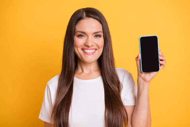 Photo portrait of woman demonstrating smartphone screen with empty space laughing isolated on bright yellow color background - Foto, Imagen