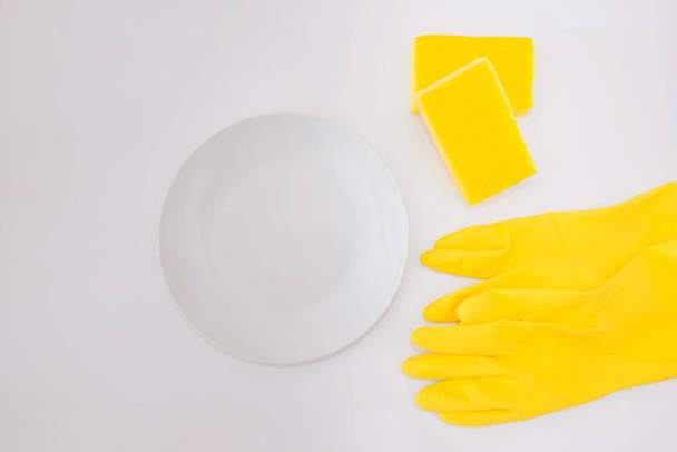 Sarı eldivenli beyaz tabak ve beyaz arka planda sarı bez. Uzayı kopyala Yukarıdan görüntüle. - Fotoğraf, Görsel