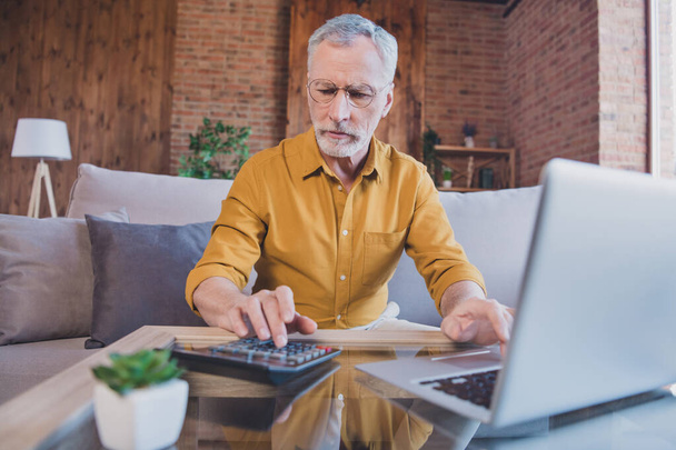 Photo of strict elder white hair man work laptop sit wear spectacles yellow shirt at home alone - Fotografie, Obrázek