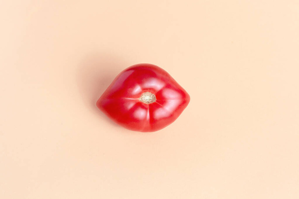 Tomato in the form of lips, smiles on a beige background. Humor, joke. Beauty concept. - Foto, afbeelding