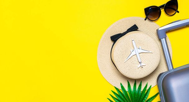 Summer time. Travel accessories with suitcase, white plane, palm leaves in minimal trip vacation concept on yellow background. Exotic tropical beach with copy space - Photo, Image
