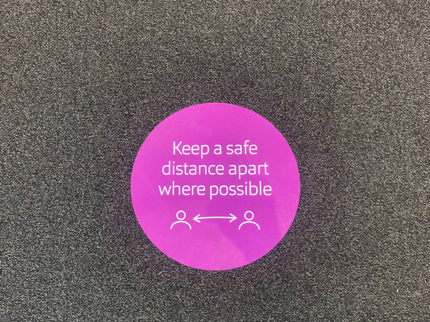 Знак на підлозі каже: "Збережіть безпечну дистанцію, якщо це можливо" під час пандемії Коронавірусу. - Фото, зображення