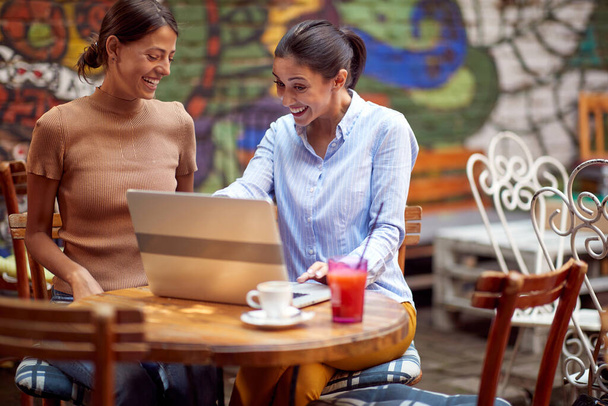young adult caucasian woman showing something on her laptop to her female friend, smiling - Foto, imagen