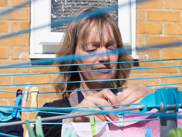 Una dama cuelga la ropa en una secadora giratoria en un día soleado.Visto a través de líneas de ropa que cruzan  - Foto, imagen