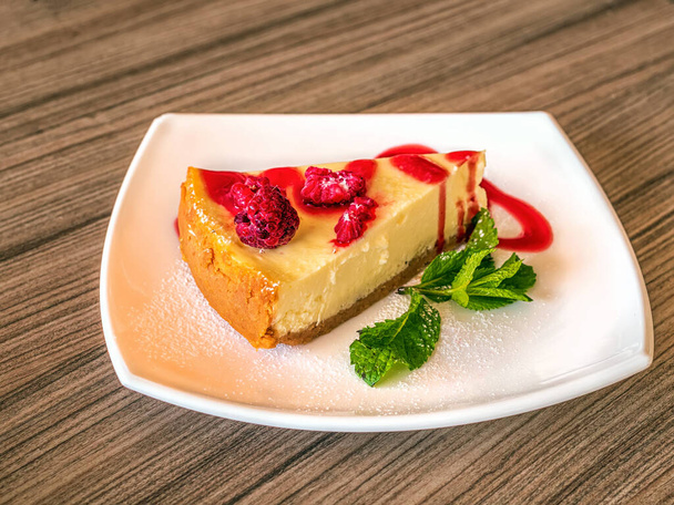White plate with a cheesecake is standing on a wooden table. Close-up. - Foto, Imagem